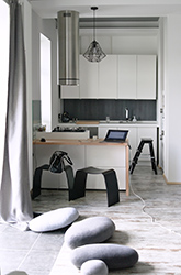 View to the kitchen island and the kitchen with floor pillows shaped as pebbles. Jorgen Moller Askman chairs in black add to the overall Zen look.