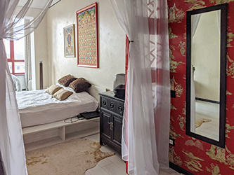 Red boudoir walls with Geishas complement red room divider, red window frames and red Tibetan art pieces. Another oriental cabinet is right next to the bed. Hide carpets also quote Tibetan tradition to meditate on animal hides.